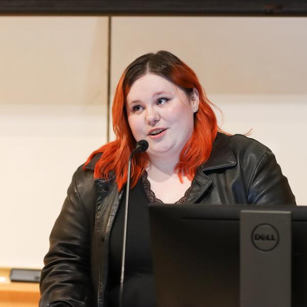 A student stands in front of a microphone in a classroom.