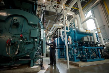 a power engineer inspects large tanks in a big machine room with sunlight peeking through the window