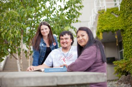 Three students chat around a table outside