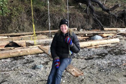 Christin Collishaw sitting outside in a swing at beach and smiling at the camera