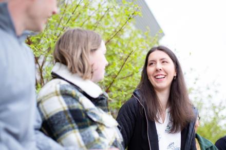 A young woman with long dark hair laghing with friends.