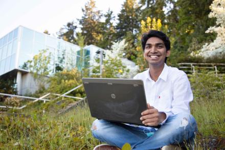 Student typing on laptop outside