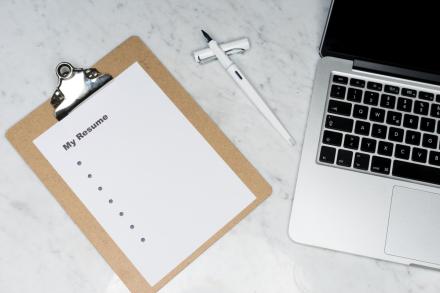 A clipboard the says "My Resume" with bullet points rests next to a laptop 